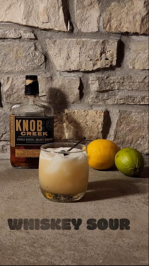 Knob Creek bottle with a whiskey sour cocktail