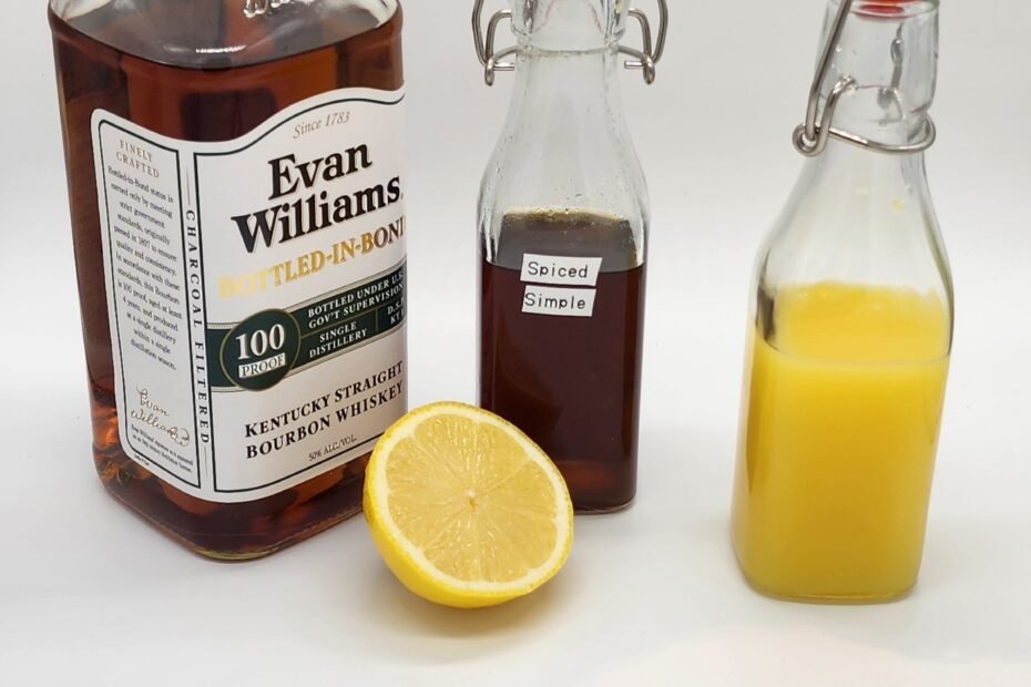 bourbon bottle with orange juice a lemon and a bottle of spiced honey syrup
